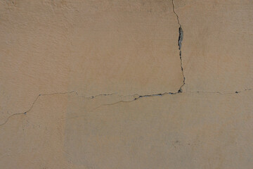 A fragment of the wall with beige paint with a small crack descends vertically down and goes to the left side of the frame. Factors of destruction in construction.