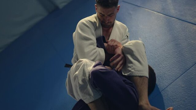 Jiu jitsu training sparring athlete fighter applying kimura or americana shoulder lock submission on his opponent during technique practice. Slow-motion shot