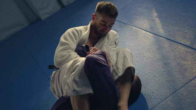 Professional jiu jitsu figter athlete training on sparring holding kimura lock submission on the opponents arm wearing kimono
