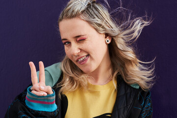 Portrait, woman tongue and peace sign with wink for y2k fashion and silly by dark background. Gen z...