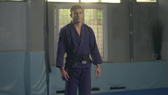 Jiu jitsu fighter in blue kimono standing on the mat and looking in the camera