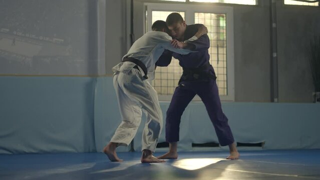 Karatekas legs fighting in gym. Handheld shot of karate fighters in blue and white kimonos practicing karate, preparing for competition, improving skills