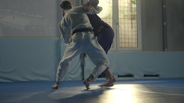 Tilt down shot of male martial arts performing takedown while having jiu-jitsu workout in gym. Slow-motion shot
