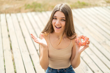 Teenager girl holding a donut at outdoors with shocked facial expression
