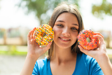 Teenager girl at outdoors holding donuts with happy expression
