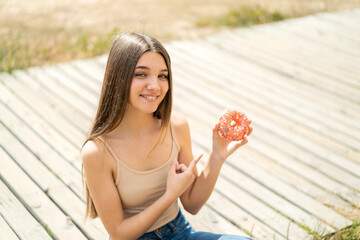 Teenager girl holding a donut at outdoors and pointing it