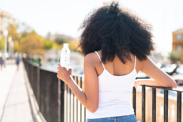 Young African American woman with a bottle of water at outdoors in back position