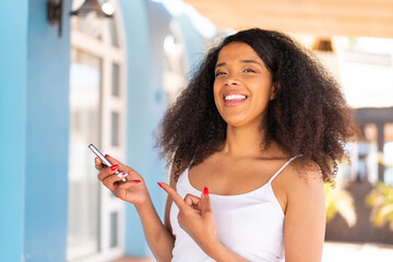 Young African American woman using mobile phone at outdoors and pointing it