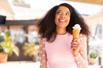 Young African American woman with a cornet ice cream at outdoors looking up while smiling