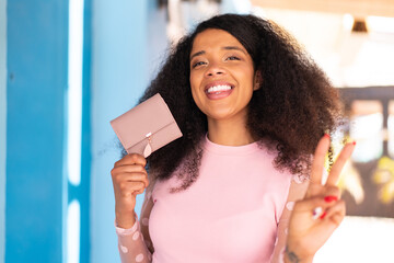 Young African American woman holding a wallet at outdoors smiling and showing victory sign