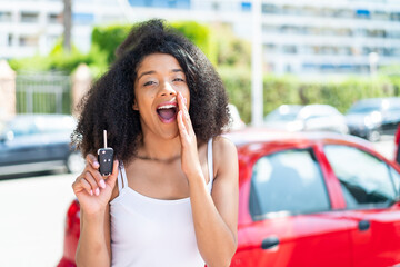 Young African American woman holding car keys at outdoors shouting with mouth wide open