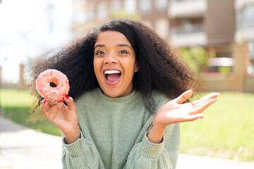 Young African American woman holding a donut at outdoors with shocked facial expression