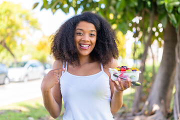 Young African American woman holding a bowl of fruit at outdoors with surprise facial expression