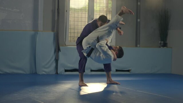 Professional male martial art fighter throwing his opponent and fighting with him in gym during jiu-jitsu training session