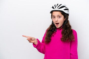 Little cyclist girl isolated on white background surprised and pointing finger to the side