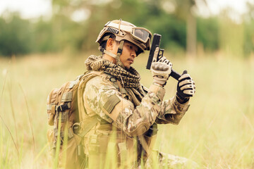 Amidst a perilous battlefield, an army soldier, prepared for combat, holds a pistol ready to fire,...