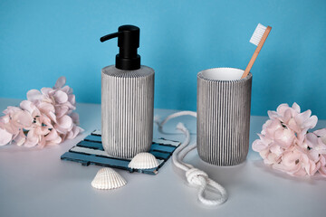 Modern Bathroom Decor with Soap Dispenser and Toothbrush Holder in Minimalist Style on Blue Background with Pink Flowers and sea shells.
