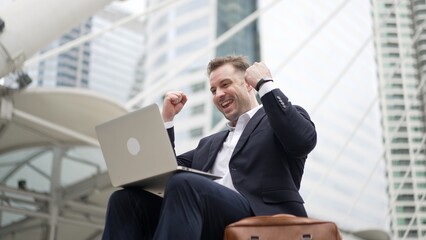 Low angle view of professional business man working on laptop at stairs while celebrate successful...