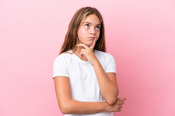 Little caucasian girl isolated on pink background having doubts while looking up