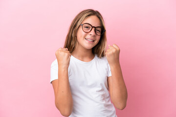 Little caucasian girl isolated on pink background With glasses and celebrating a victory