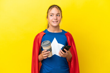 Super Hero little girl isolated on yellow background holding coffee to take away and a mobile while...