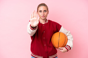 Young basketball caucasian player woman isolated on pink background making stop gesture