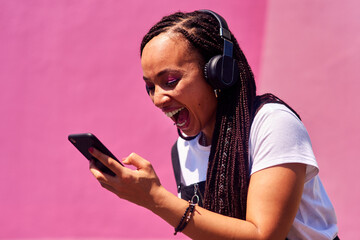Woman, pink background and happy winner with phone, celebrate for success with internet. Female...