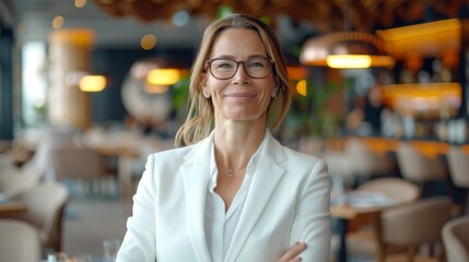A confident businesswoman in eyeglasses and a white blazer smiles at the camera in a cafe setting.