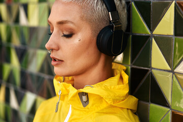 Fashion, woman and headphones at wall for streetwear, memories and calm in city. Female student,...