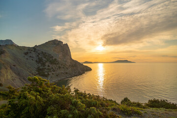 A beautiful sunset over the ocean with a rocky cliff in the background. The sky is filled with clouds, creating a serene and peaceful atmosphere.