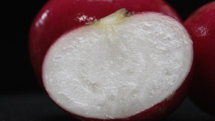A close-up of a sliced fresh radish explodes against a black background. Vibrant red flesh, a...