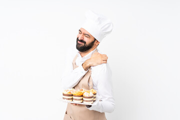 Young man holding muffin cake over isolated white background suffering from pain in shoulder for...
