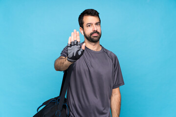 Young sport man with beard over isolated blue background making stop gesture