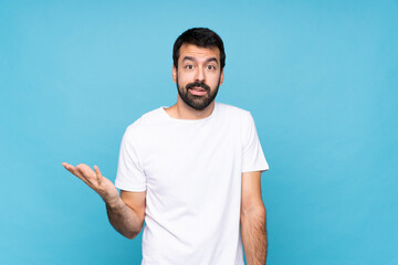 Young man with beard  over isolated blue background making doubts gesture