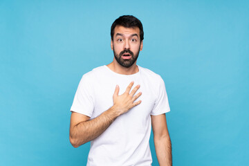 Young man with beard  over isolated blue background surprised and shocked while looking right