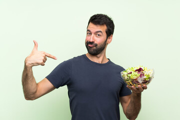 Young handsome man with salad over isolated green wall proud and self-satisfied