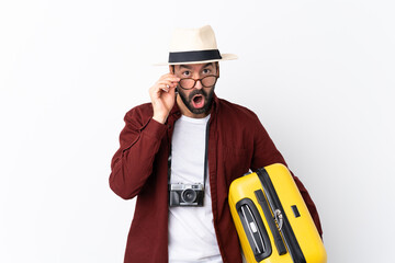 Traveler man man with beard holding a suitcase over isolated white background with glasses and...