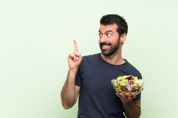 Young handsome man with salad over isolated green wall intending to realizes the solution while...