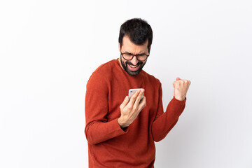 Caucasian handsome man with beard over isolated white background with phone in victory position