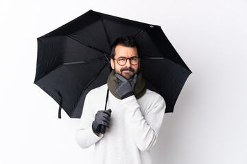 Caucasian handsome man with beard holding an umbrella over isolated white wall thinking
