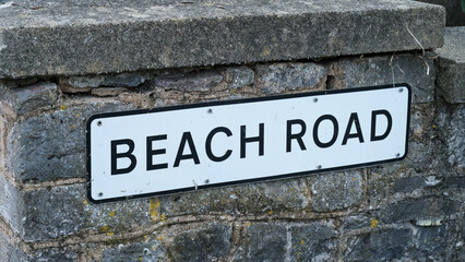 Close up of street signpost for Beach Road on stone wall at popular holiday destination