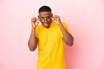 Young latin man isolated on pink background with glasses and surprised