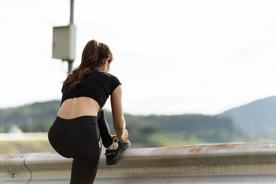 Healthy woman warms up before jogging and relaxes. Stretch your arms and look outside at the road, get in shape at the park before running and enjoy healthy outdoor activities.
