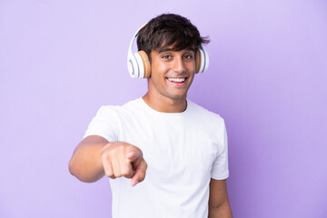Young caucasian man isolated on purple background listening music