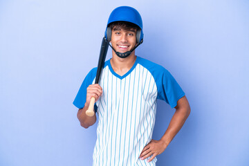 Baseball caucasian man player with helmet and bat isolated on blue background posing with arms at hip and smiling