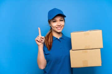 Delivery girl over isolated blue wall showing and lifting a finger in sign of the best