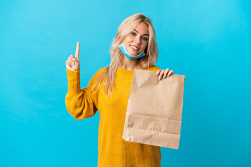 Young Russian woman holding a grocery shopping bag isolated on blue background showing and lifting...