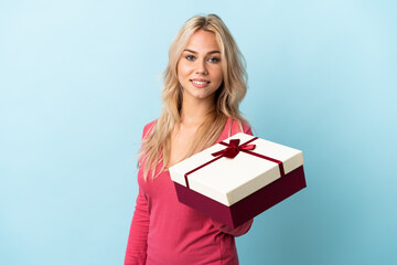 Young Russian woman holding a gift isolated on blue background smiling a lot