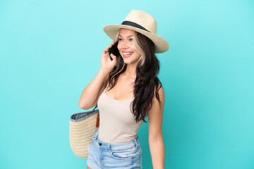 Fototapeta premium Teenager Russian girl with pamel and beach bag isolated on blue background keeping a conversation with the mobile phone