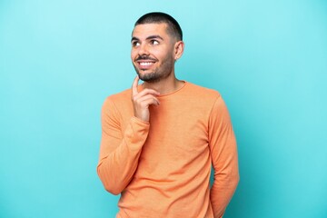 Young caucasian man isolated on blue background looking up while smiling